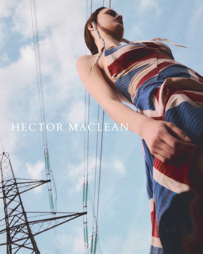 Low angle fashion portrait of a woman wearing a dress with a Union Jack pattern against a blue sky and electrical towers.
