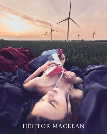 Woman in a field with wind turbines at sunset, wearing colorful fabric, lies on a bed of fabric under a vibrant sky.