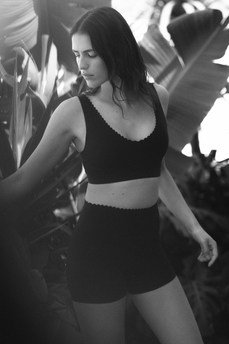 Monochrome portrait of a woman in a two-piece outfit surrounded by tropical plants, showcasing fashion and nature elements.