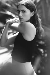 Monochrome portrait of model Adele Aldighieri wearing a dark tank top while stretching her shoulder outdoors.