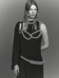 Model wearing a black draped dress accented with thick crystal ropes against a seamless grey backdrop.