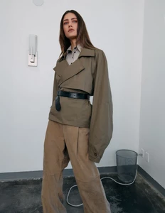 Model wearing an olive cropped trench coat and beige trousers against an office background for Mirror Mirror Magazine