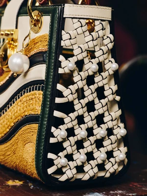 Close-up detail of a Dior Lady Art handbag featuring woven off-white leather lattice with pearls, gold hardware, and textured embroidery.