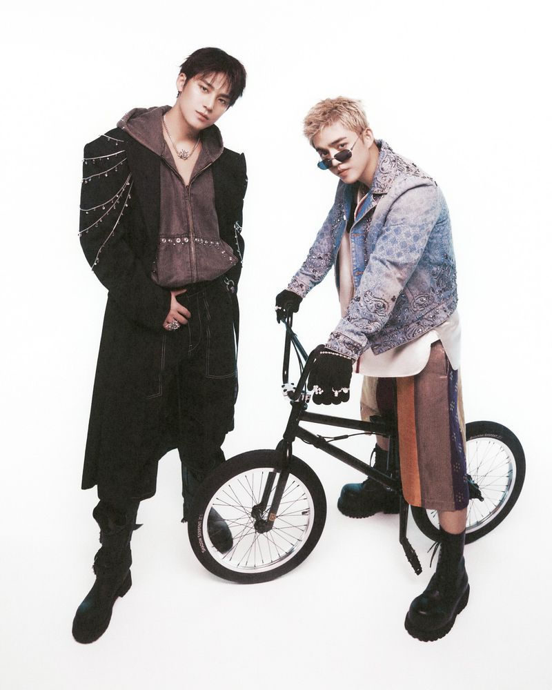 Two adult men pose next to a BMX bike in a studio shot, wearing streetwear fashion against a white backdrop, showcasing a trendy, casual style.