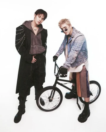 Two adult men pose next to a BMX bike in a studio shot, wearing streetwear fashion against a white backdrop, showcasing a trendy, casual style.