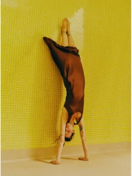 Model Waleska Gorczevski doing a handstand against a yellow tiled wall in a brown slip dress