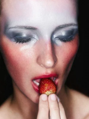 Close-up portrait of a woman with dramatic makeup holding a fresh strawberry to her lips for Vogue Brasil by Hick Duarte.