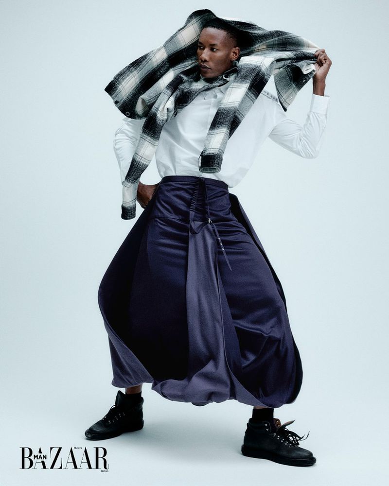 Fashion shot of a person in a white shirt, navy skirt, boots, and a black and white plaid scarf, standing in a light grey studio.