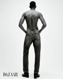 Shirtless man seen from behind wearing dark denim jeans and black boots against a plain white background for Harper's Bazaar Brazil