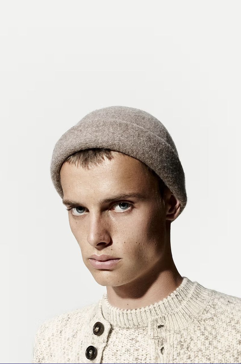 Headshot of a young adult male wearing a grey beanie hat and a light colored sweater, photographed in a photo studio.