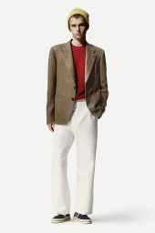 Model in a brown blazer, red sweater, white trousers, and yellow beanie against a plain white background