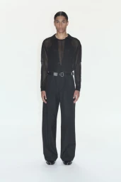 Model wearing a black sheer button-down shirt and black trousers against a plain white background