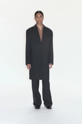 Model wearing a long black coat and trousers against a plain white background for 032c Spring/Summer 2026.