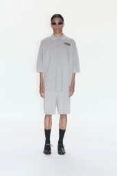 Model wearing a grey polo shirt and matching shorts with dark sunglasses against a seamless white background.