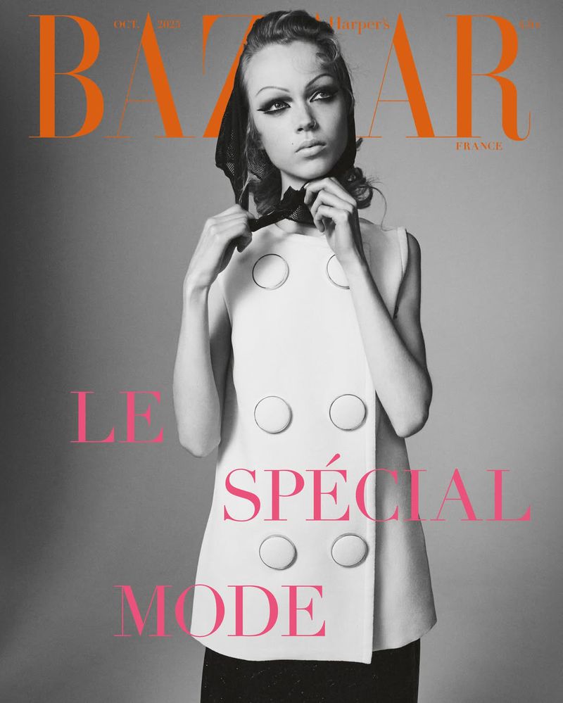 Fashion magazine cover featuring a model in a white dress with large buttons, accessorized with a black scarf and heavy eye makeup.