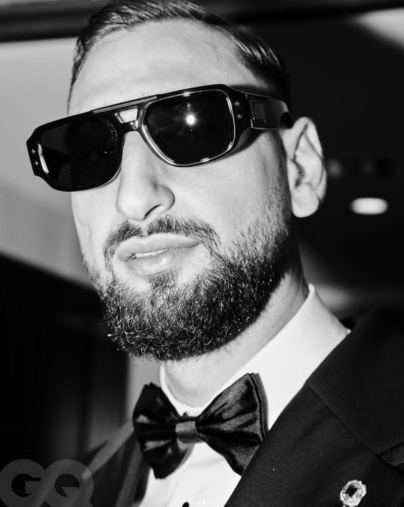 Headshot in black and white of a bearded adult male wearing sunglasses and a bow tie looking directly at the camera.