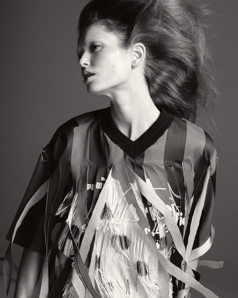 Monochrome studio portrait of a woman with dramatic hair wearing a black and striped top with white fringed embellishments. Fashion shot.