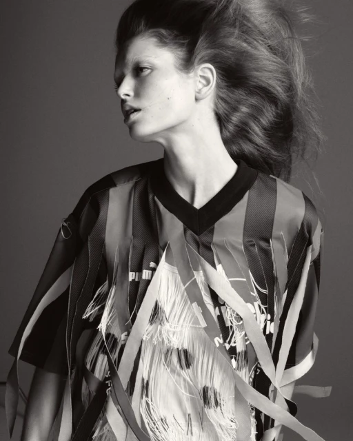 Monochrome studio portrait of a woman with dramatic hair wearing a black and striped top with white fringed embellishments. Fashion shot.