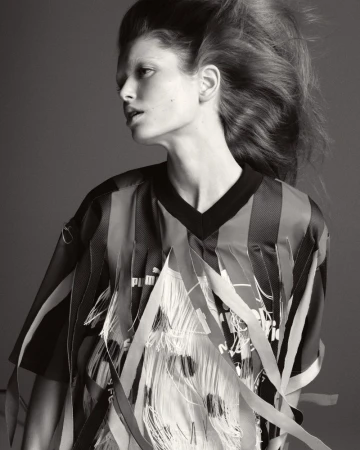 Monochrome studio portrait of a woman with dramatic hair wearing a black and striped top with white fringed embellishments. Fashion shot.