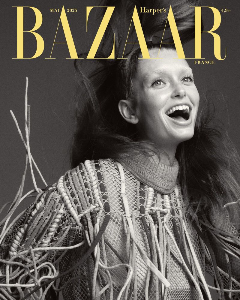 Black and white magazine cover featuring a smiling woman with flowing hair and a textured, fringed top against a dark background.