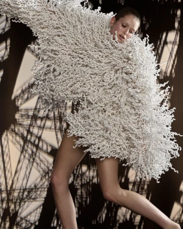 Model wearing an oversized textured white fringed garment with the Eiffel Tower structure behind in Harper's Bazaar France.