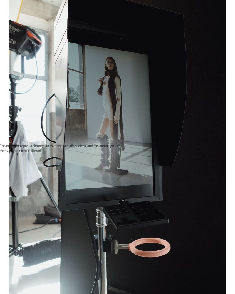 Behind-the-scenes shot of fashion photo shoot setup in a studio with a model's image displayed on a large monitor.