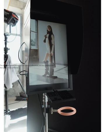 Behind-the-scenes shot of fashion photo shoot setup in a studio with a model's image displayed on a large monitor.