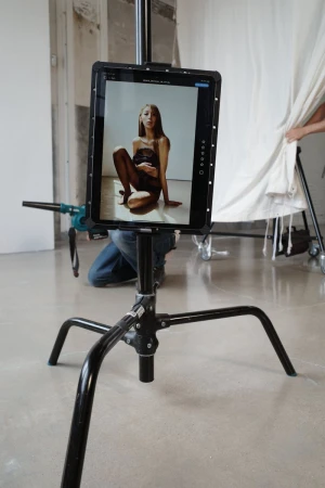 Image on a tablet shows a model sitting on the floor, captured in a studio setting with a white backdrop.