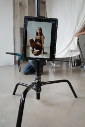 Tablet on a black metal C-stand displaying a fashion shoot image in a minimalist studio setting.