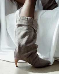 Close-up of a slouchy grey textile boot with kitten heel against a white draped backdrop