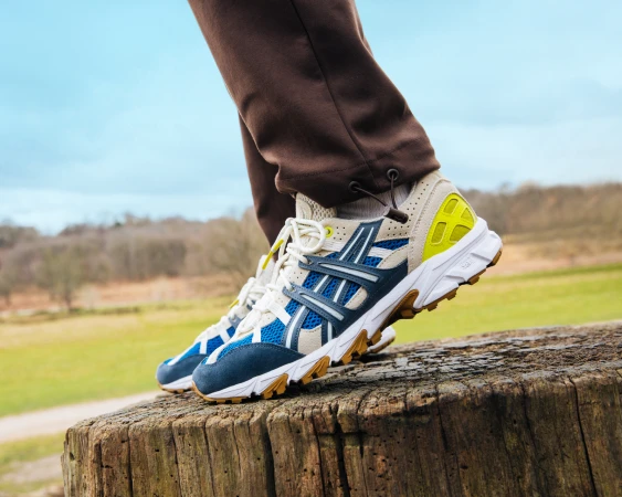 Eye-level, close-up shot capturing athletic shoe on a tree stump outdoors against a soft, blue sky and a blurred background of green grass.
