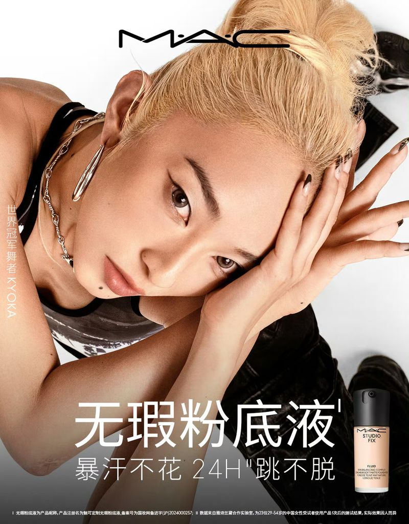 Close-up of a fair-skinned adult woman with blonde hair in a high bun, silver jewelry, and a mole on her cheek posing near makeup.