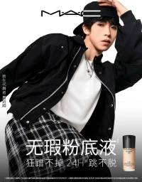 Young man wearing a black baseball cap, black bomber jacket, white t-shirt, and plaid skirt in a dynamic pose for MAC Cosmetics.