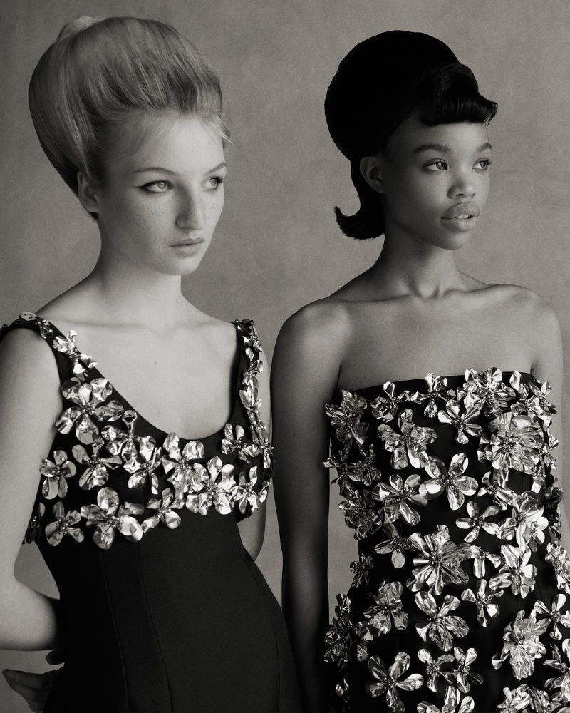 Two women with stylized retro hairstyles and dresses with floral embellishments, captured in a monochrome portrait, fashion-forward.