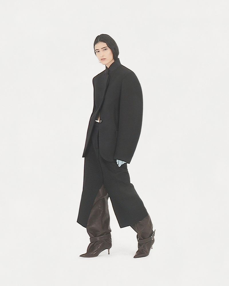 Fashion shot of woman in oversized black blazer and baggy pants, paired with brown leather heeled boots against a white backdrop.