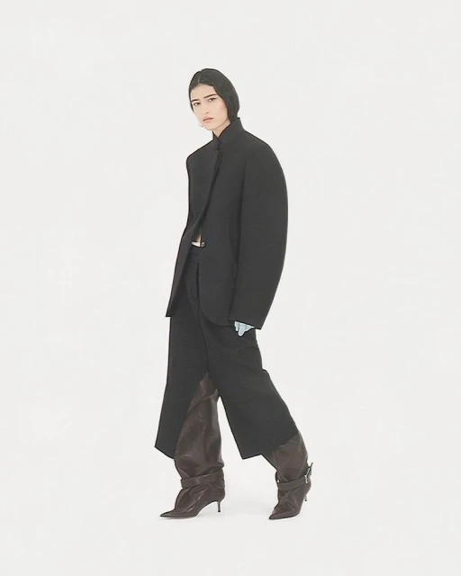 Fashion shot of woman in oversized black blazer and baggy pants, paired with brown leather heeled boots against a white backdrop.