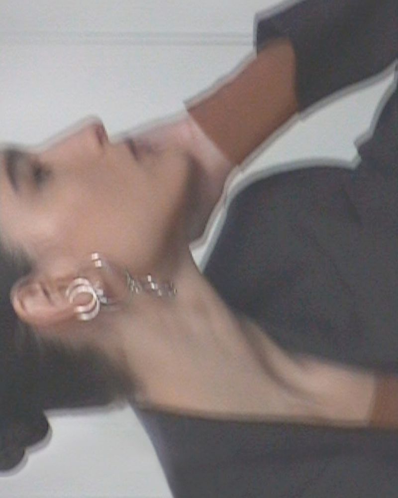 Profile of an adult female with dark hair wearing hoop earrings and a dark blazer, set against a blurred, light-colored background.