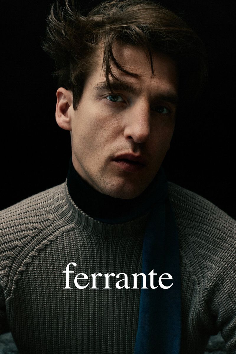 Close-up studio shot of a young adult male wearing a gray knit sweater and black turtleneck against a dark background with the brand name Ferrante.
