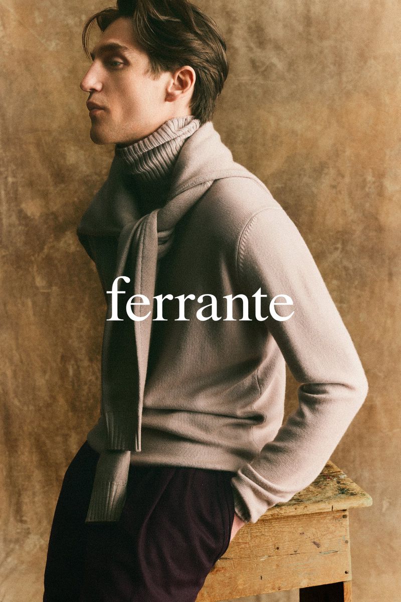 Portrait of a light-skinned male model wearing a turtleneck sweater and scarf, against a textured backdrop, promoting FERRANTE fashion.