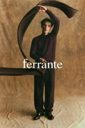 Model wearing a dark long-sleeve sweater holding a curved scarf against a textured neutral backdrop with visible brand typography