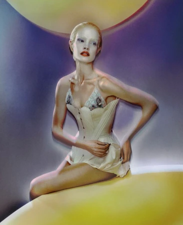 A model poses while seated, illuminated by vibrant yellow lighting. She is wearing a corset and minimal fabric against a background of blue and yellow.