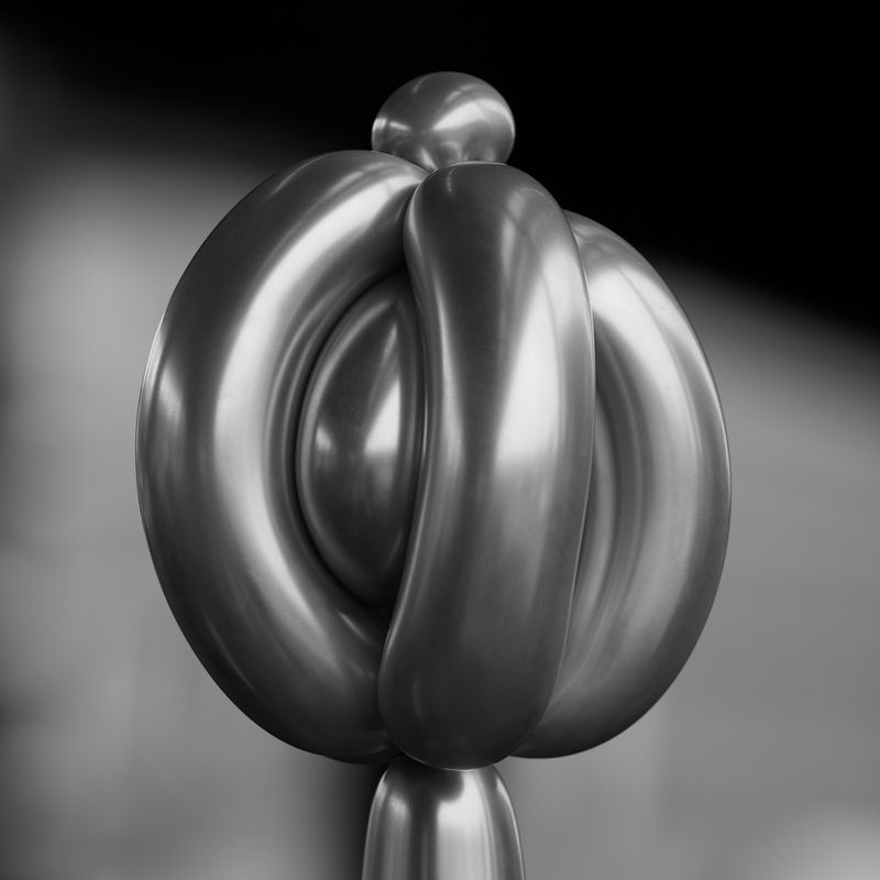 Close-up of a shiny, silver abstract sculpture with a knot-like design and spherical elements, set against a dark, blurred background.