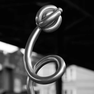 Monochrome close up of a twisted balloon sculpture shaped like a flower with a looping stem against a dark blurred backdrop.