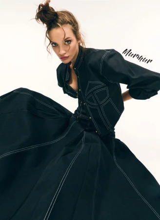 A woman poses in a black couture dress with white trim, captured in a high-angle shot against a bright backdrop, showcasing fashion and elegance.