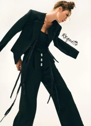 Model wearing a black blazer and matching trousers with button details against a light background