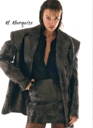 Model Carolina Bruma wears an oversized grey plaid blazer and matching miniskirt against a plain white studio background.