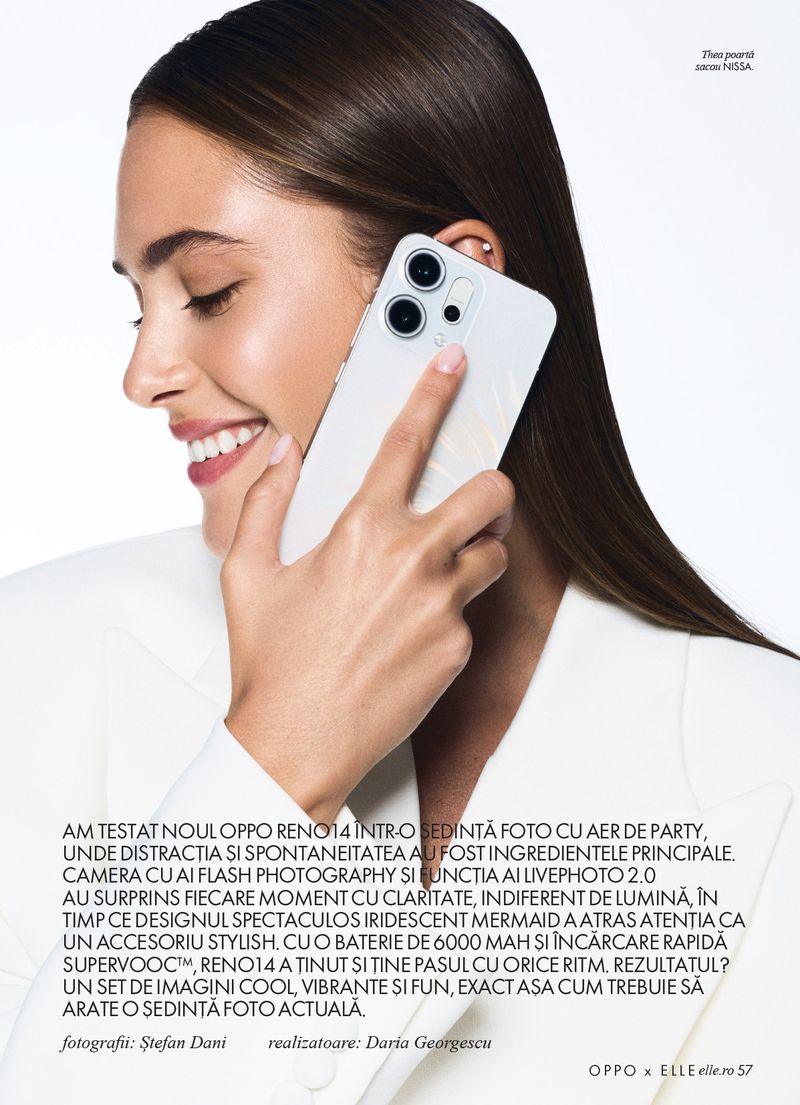 A woman in a white jacket is holding up a white smartphone with a triple-lens camera, smiling slightly. The image has clean, neutral lighting.