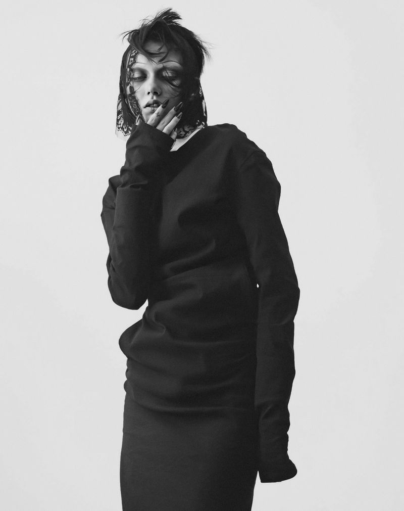 Portrait of a woman with long dark hair wearing black long sleeve shirt and black skirt in a black and white photo studio shot.