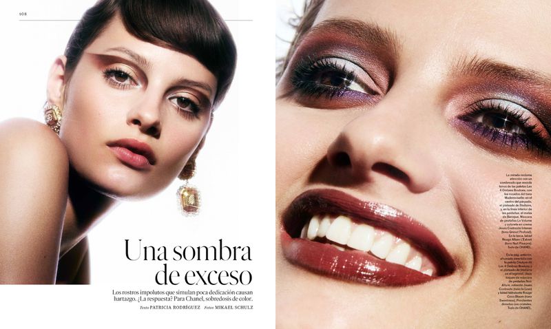 Close-up fashion beauty shot of a woman with brown hair wearing eye shadow, lipstick, and earrings against a white background.