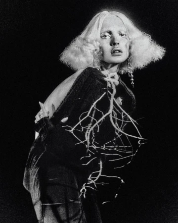 Monochrome portrait of a fashion model wearing a dark, embellished sweater against a dark background in a studio setting.